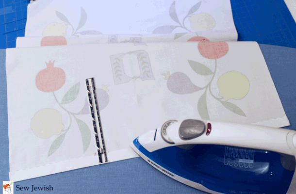 Fold 5/8” (1.6cm) of one edge to the wrong (unprinted) side of the fabric and press.